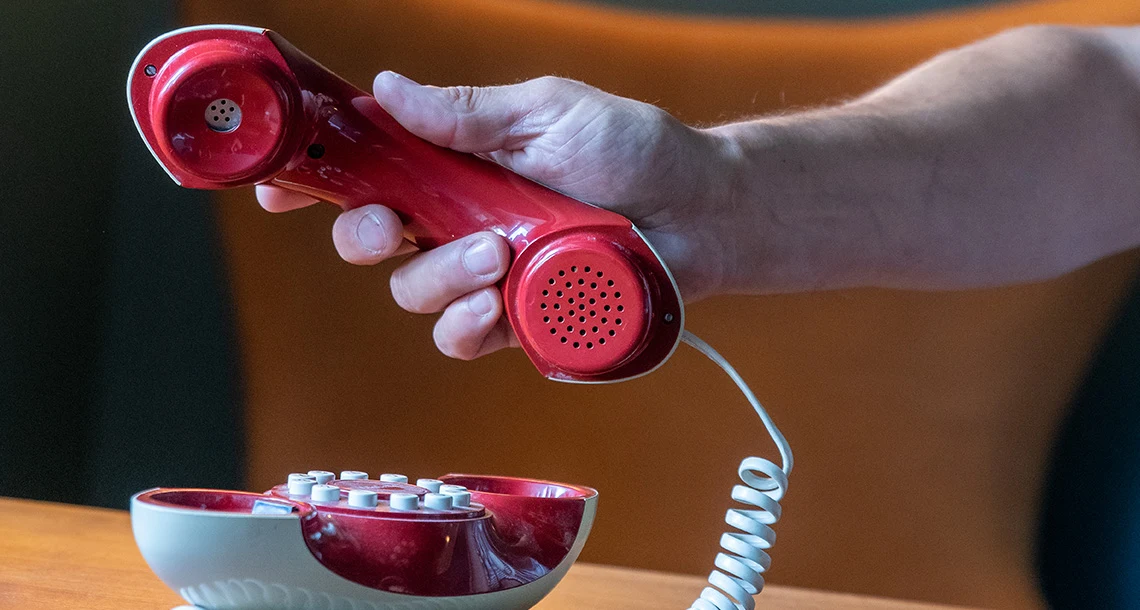 En hand håller i en röd telefonlur i retrodesign.