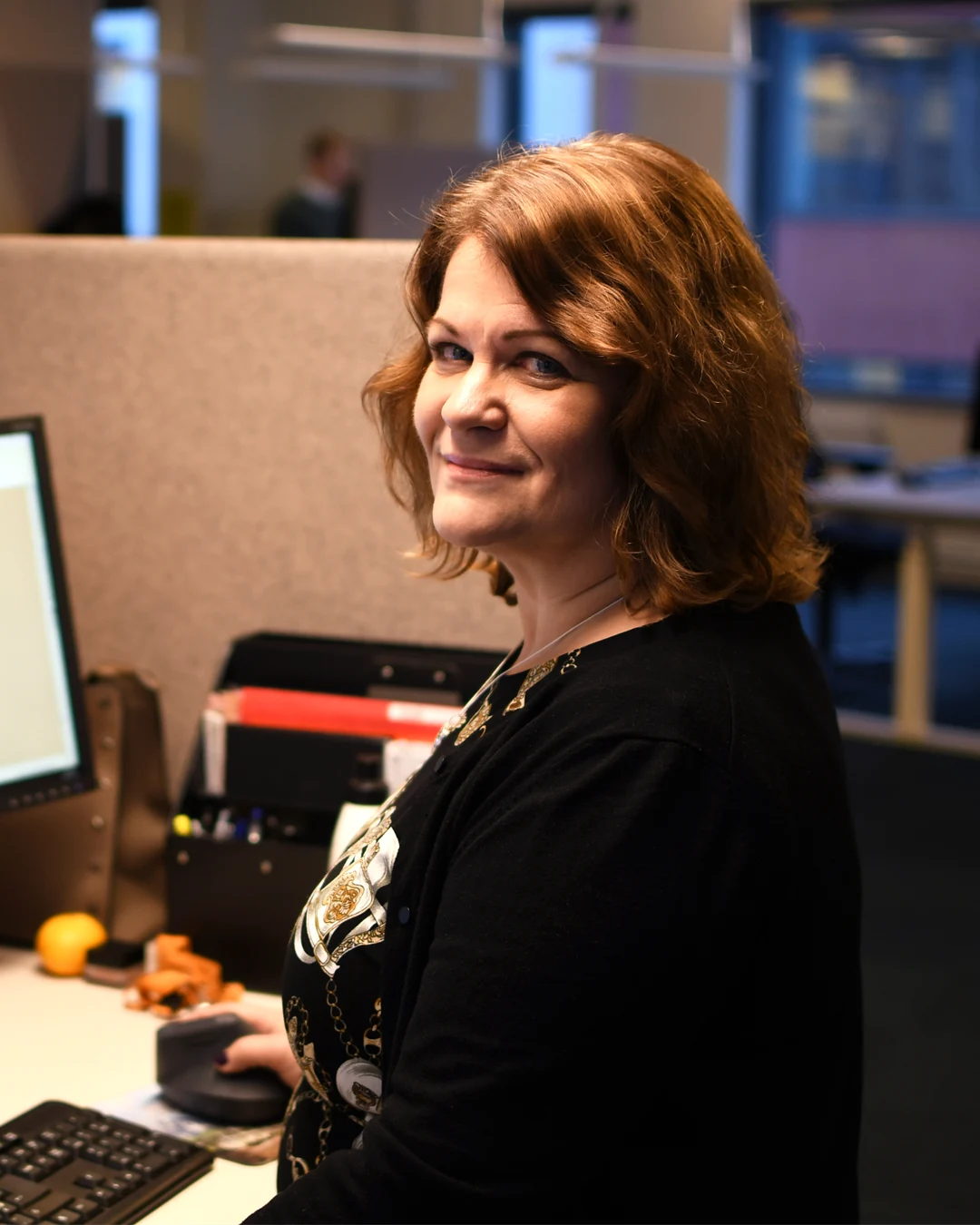 Kvinna sitter framför en datorskärm och tittar mot kameran.