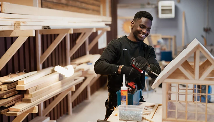 Elev i verkstadsmiljö som bygger litet modellhus i trä.