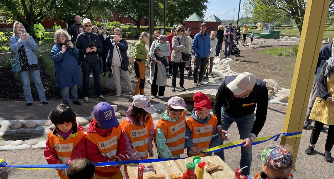 Fem barn och en vuxen klipper av ett blått och gult band med var sin sax.
