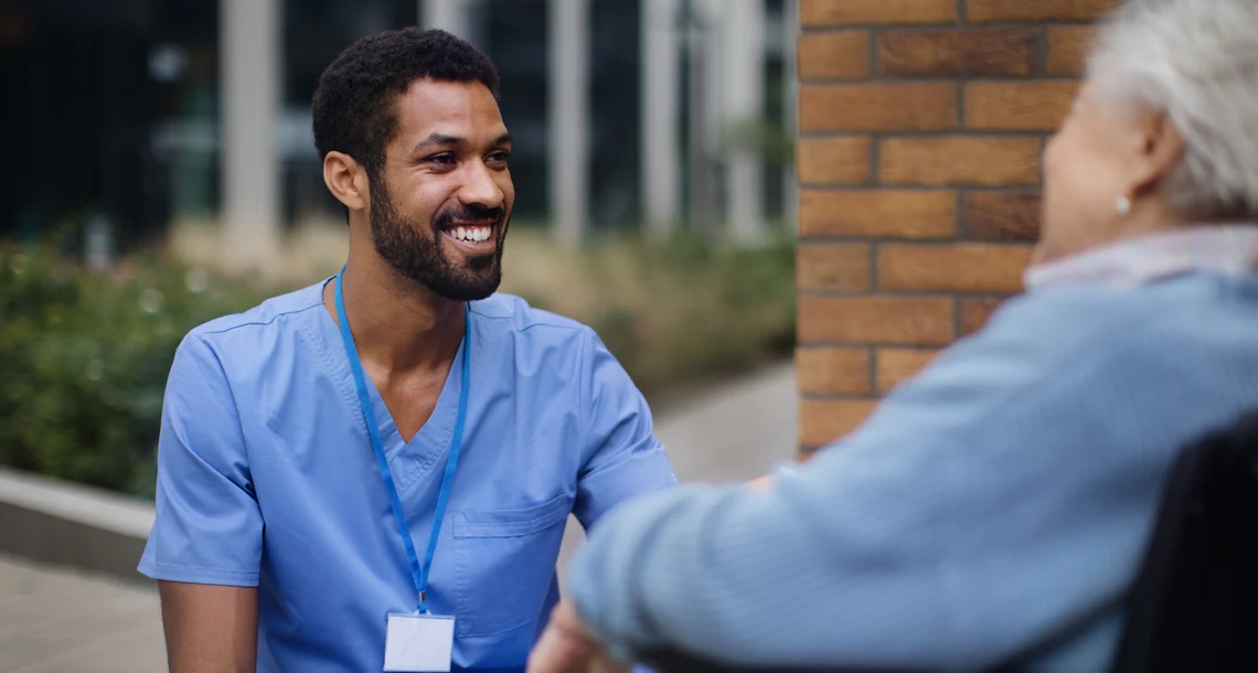 En person sitter på knä och ler mot en person som sitter i rullstol.