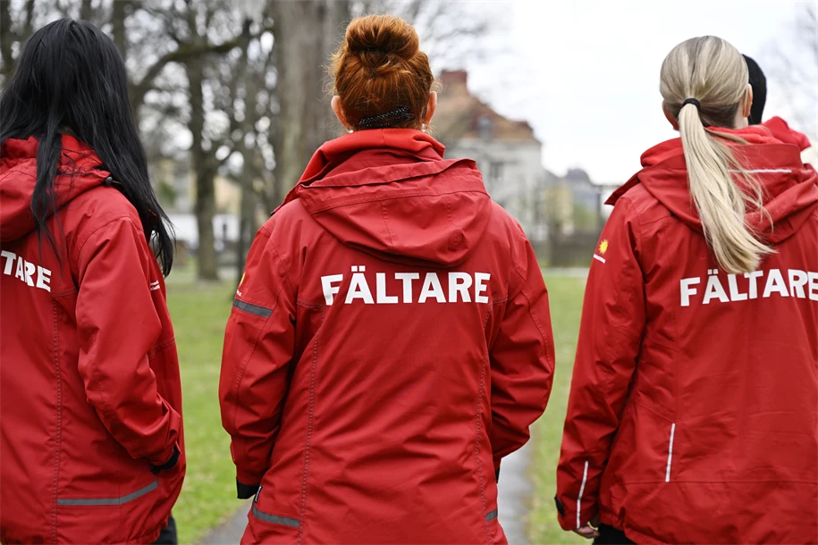 Tre fältarbetare står med ryggen mot kameran framför en majbrasa.. 