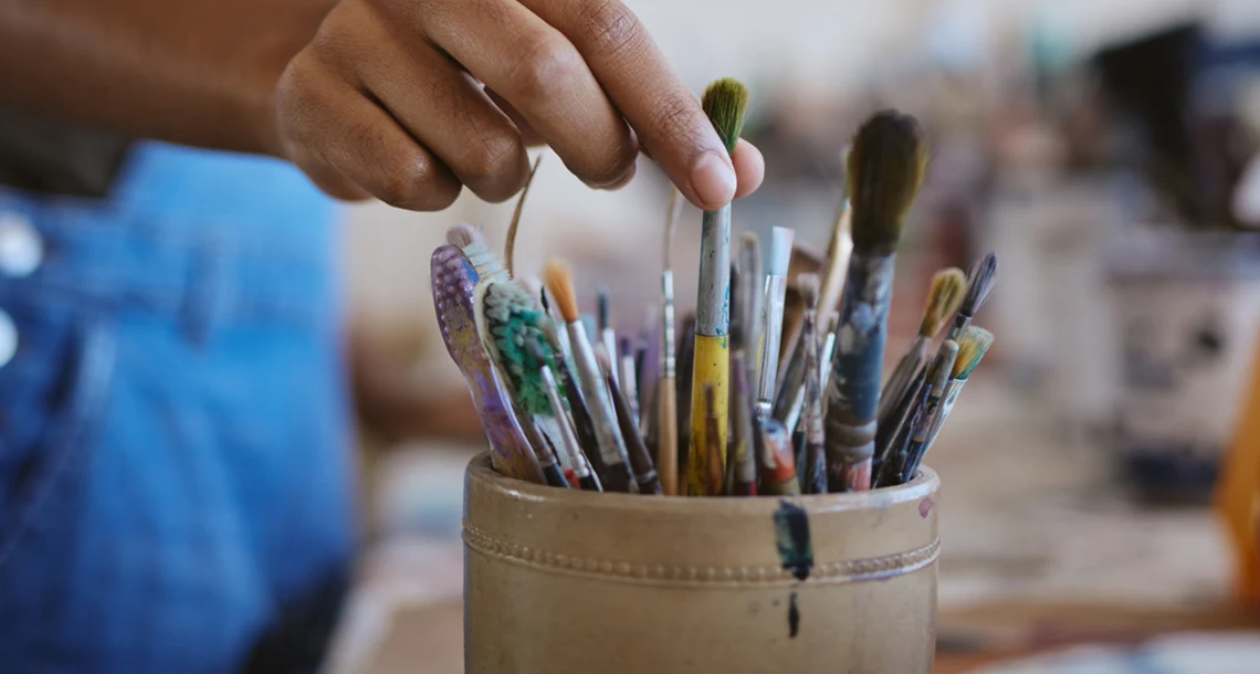 En person sträcker sig efter penslar i en burk.