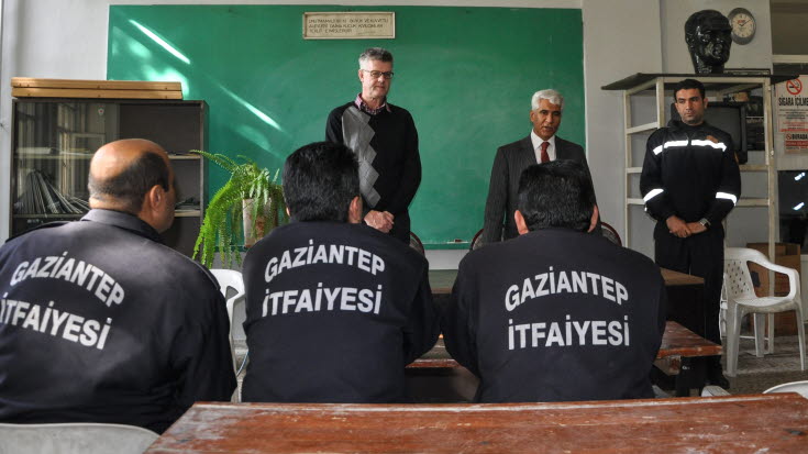 Tre män med texten Gaziantep på sina jackors rygg lyssnar på tre män som står framför dem. 