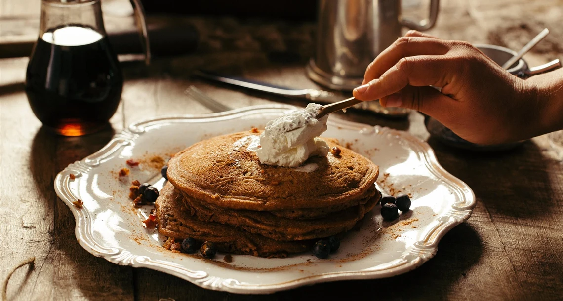 Någon klickar grädde på en hög med pannkakor på en tallrik.