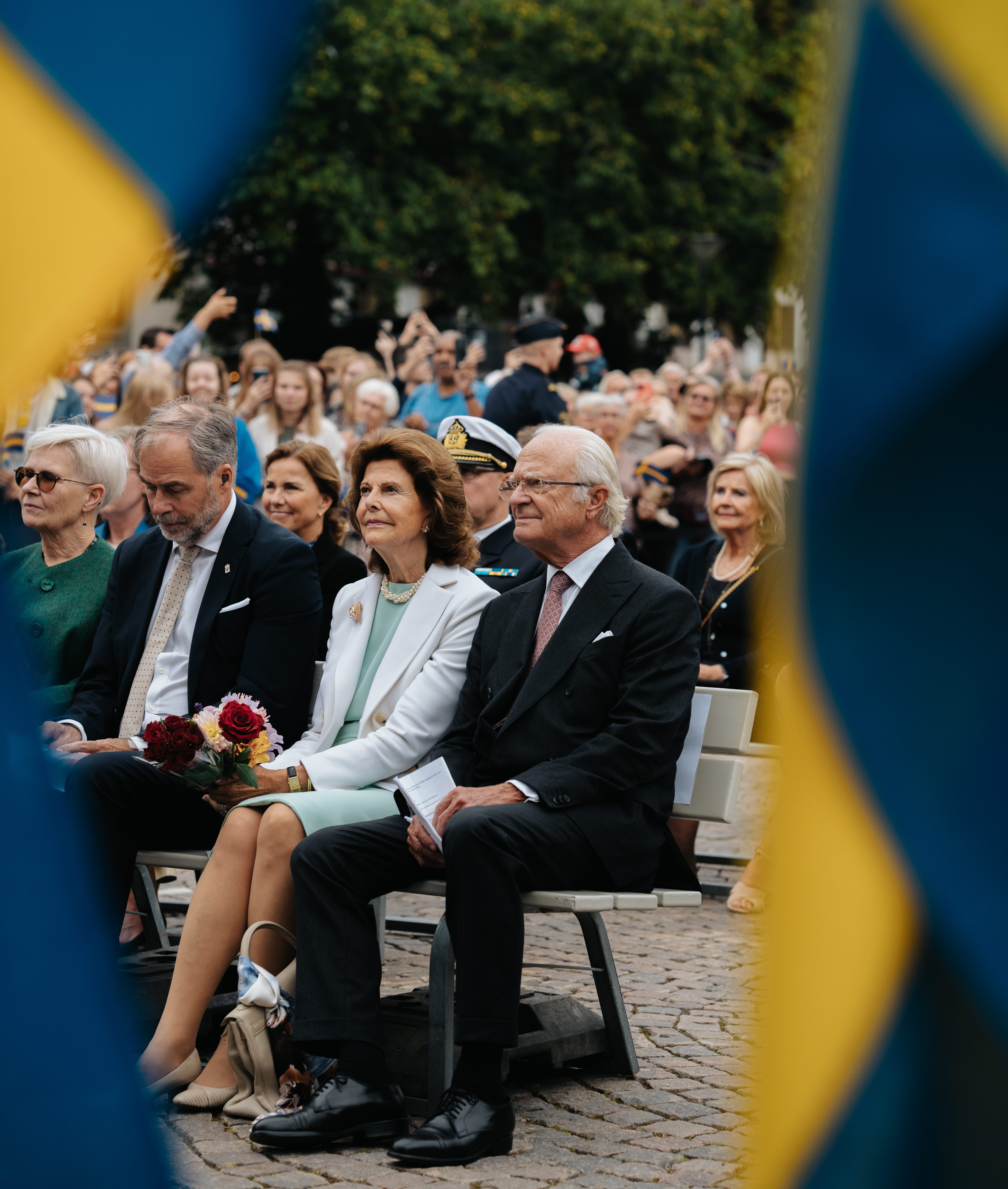 Kungen och Drottningen bakom flagga på Stora torget.