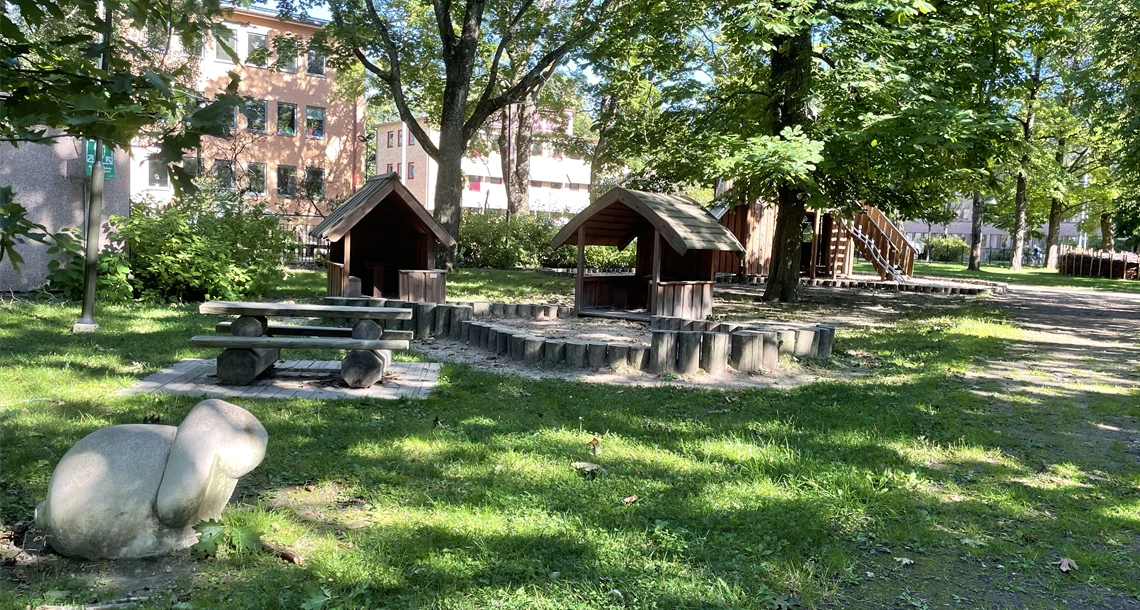 Stenfigur i form av en kanin framför två små lekhus och en klätterställning.