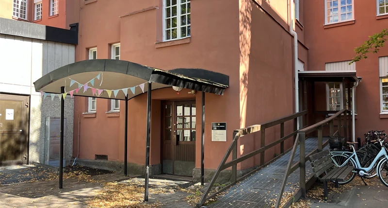 En röd byggnad med en brun dörr och rullstolsramp på höger sida