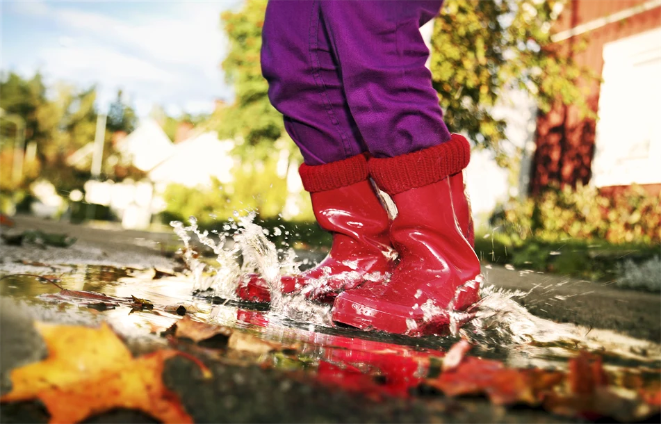 Barn med röda gummistövlar hoppas i en vattenpöl