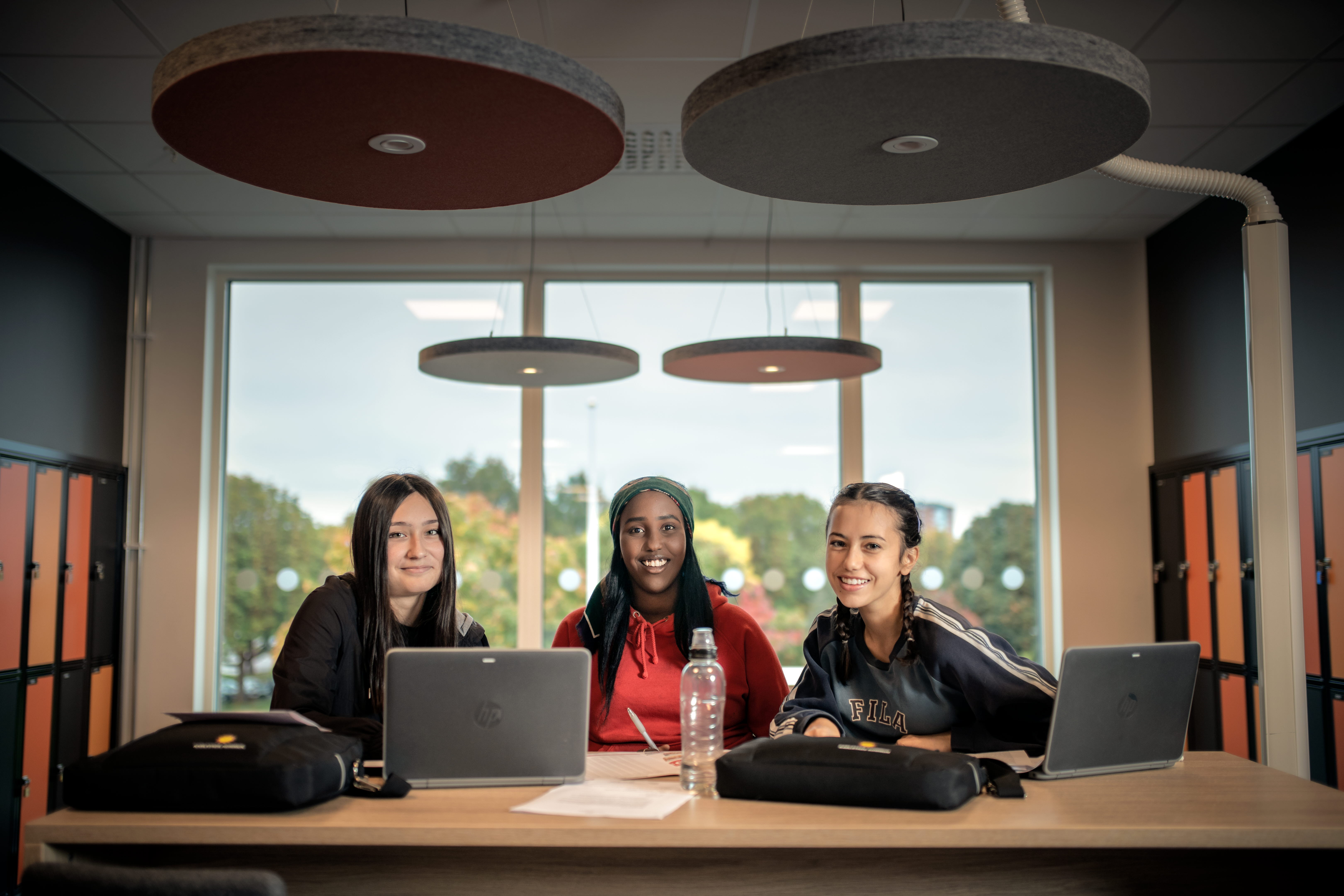 Tre elever studerar vid ett bord och ler