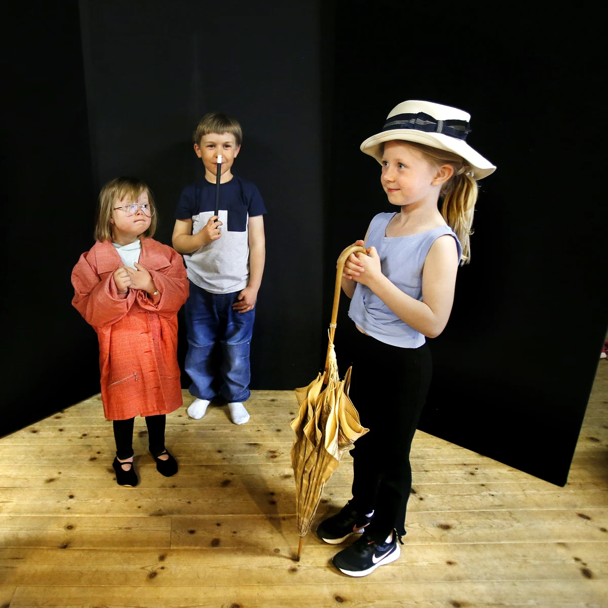 Tre barn med paraplyer, hattar och trollstavar