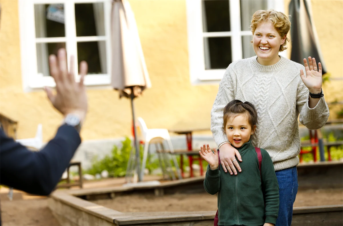 En kvinna välkomnar ett barn och en förälder till förskolan