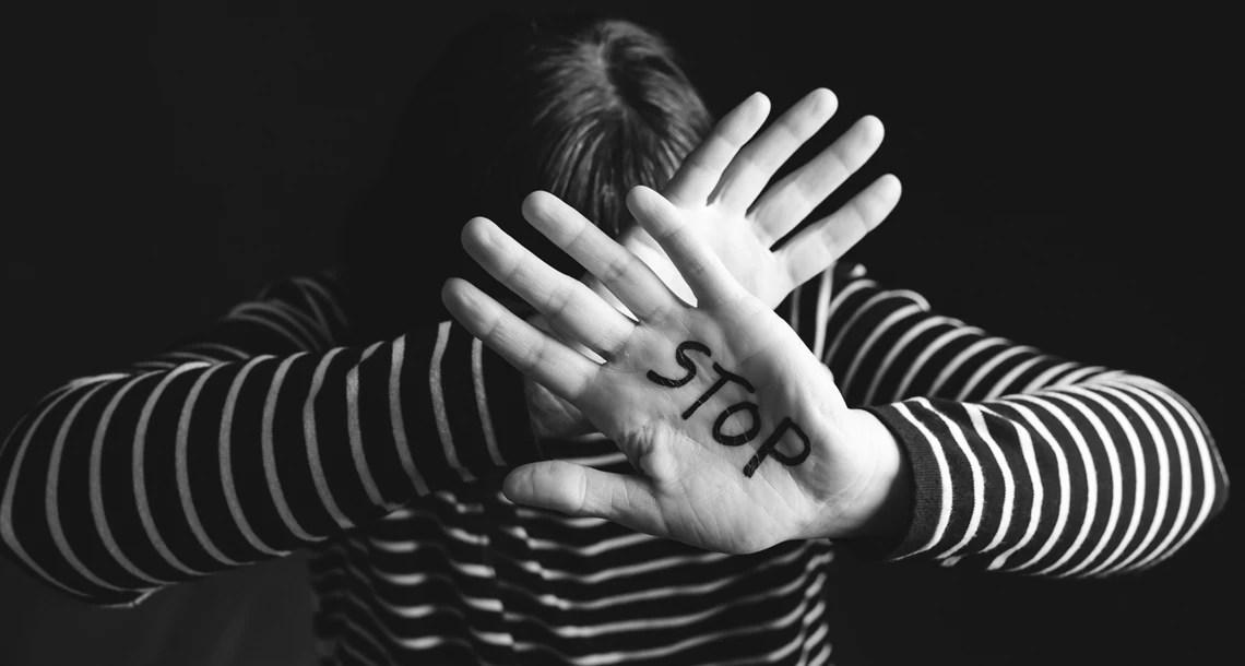 En svartvit bild. En kvinna håller händerna framför sitt huvud för att stoppa en våldsverkare. I ena handflatan är det skrivet "stop"