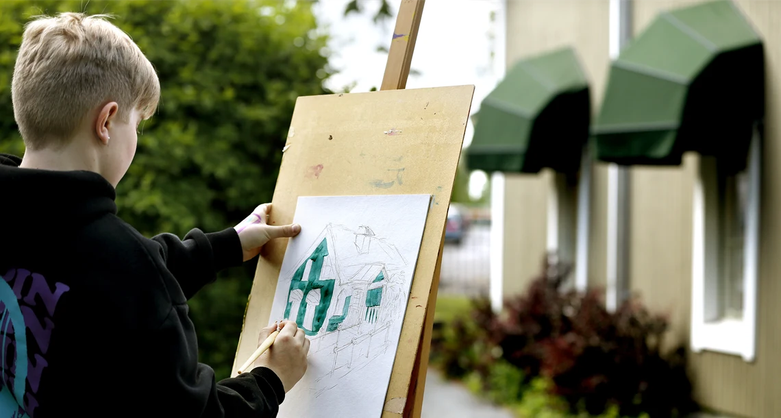 Pojke som målar ett hus på ett staffli