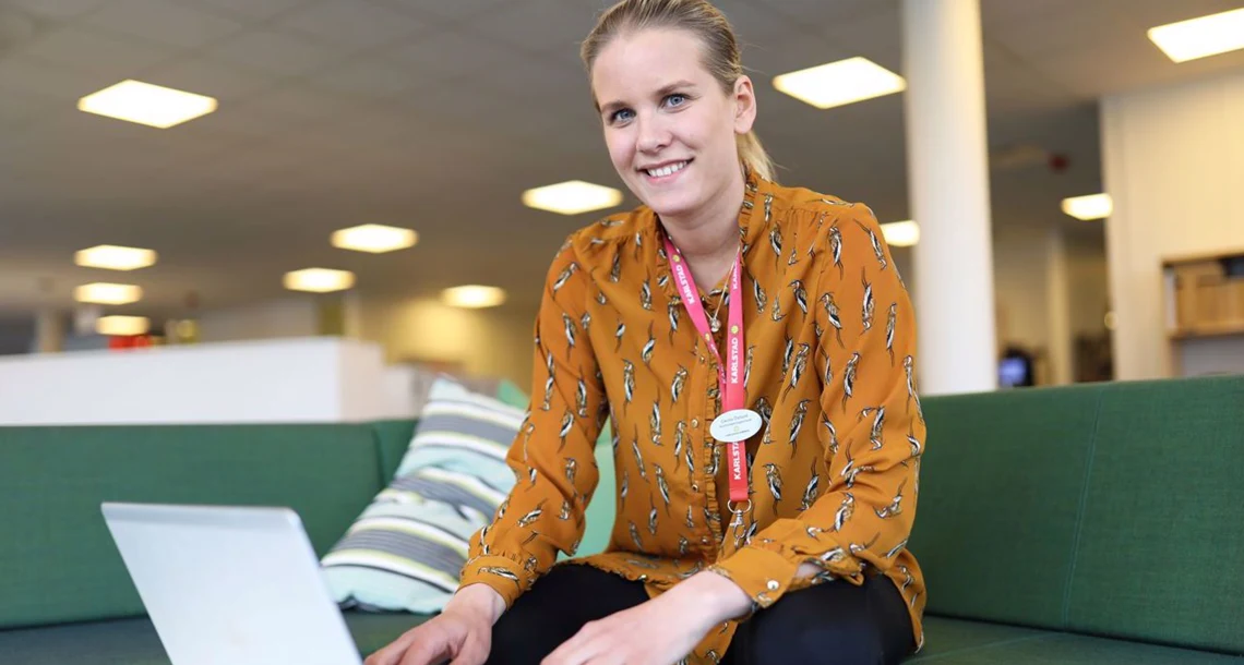 Kvinna sitter i en soffa med en laptop framför sig.