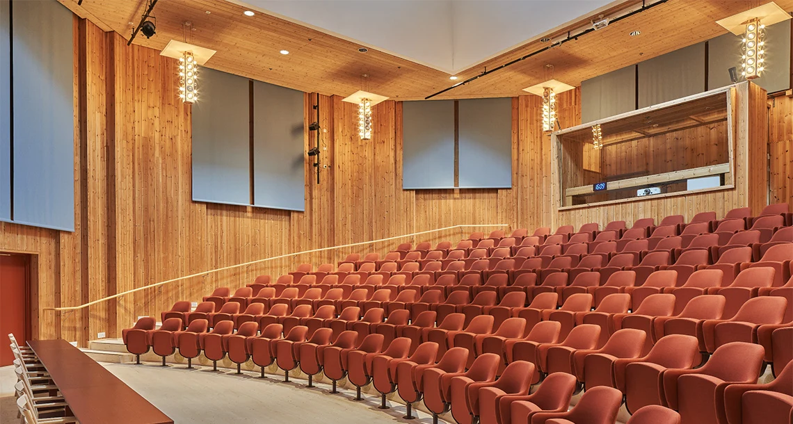 I en stor konferenslokal finns flera sluttande rader med stolar i en rödorange färg.