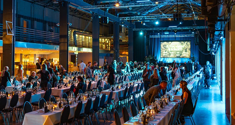 En stor lokal med högt i tak där det står långa uppdukade bord med några människor som sitter ner.