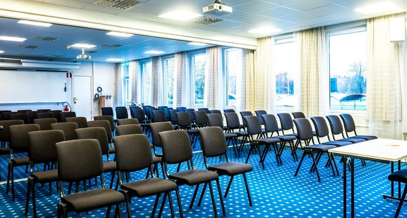 En mängd mörka stoler står uppradade i ett rum med blå heltäckningsmatta.