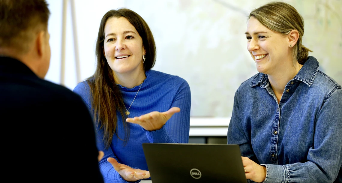 Två kvinnor gestikulerar och pratar med man som man endast ser ryggen på.