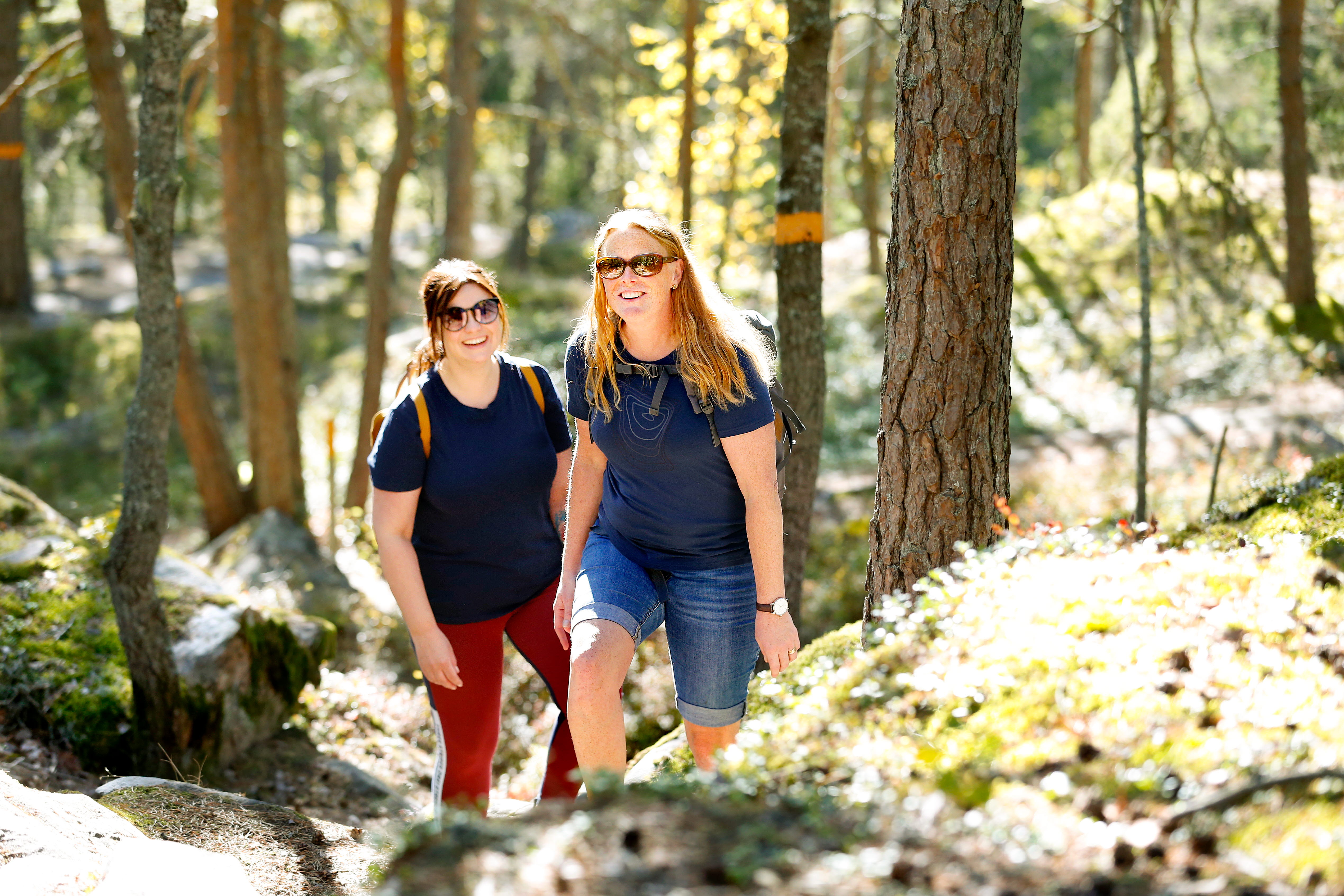 Två kvinnor vandrar bland klippblocken i I2-skogen.