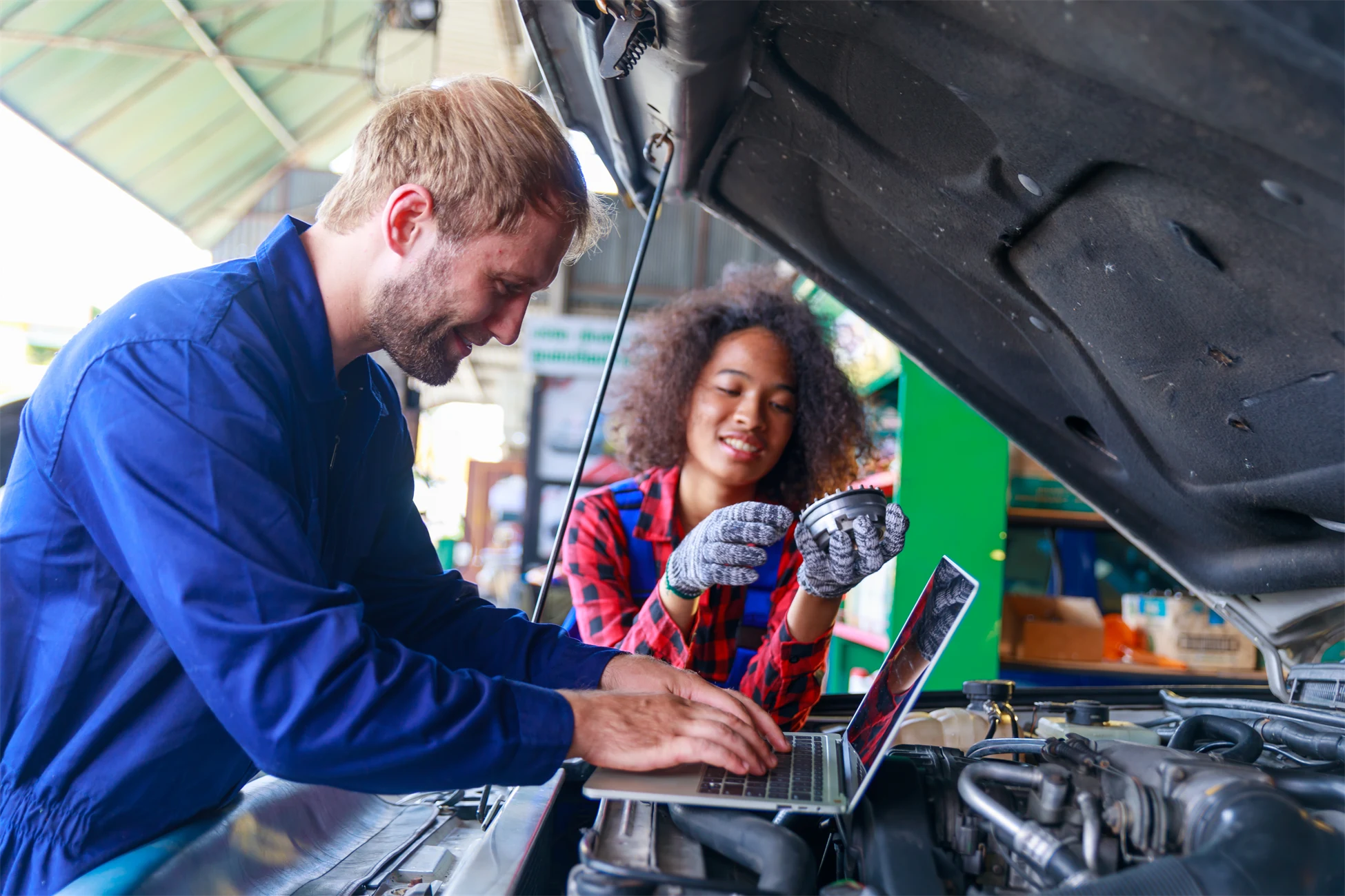 Två personer mekar med bil och använder en laptop.
