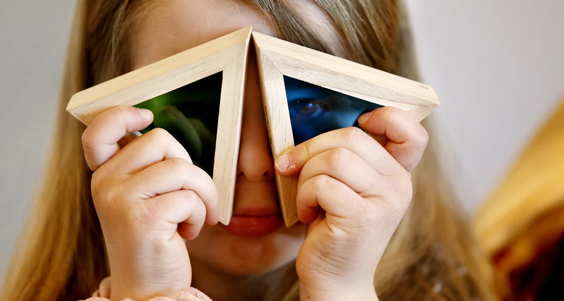 Flicka som håller två färgade trekanter för ögonen
