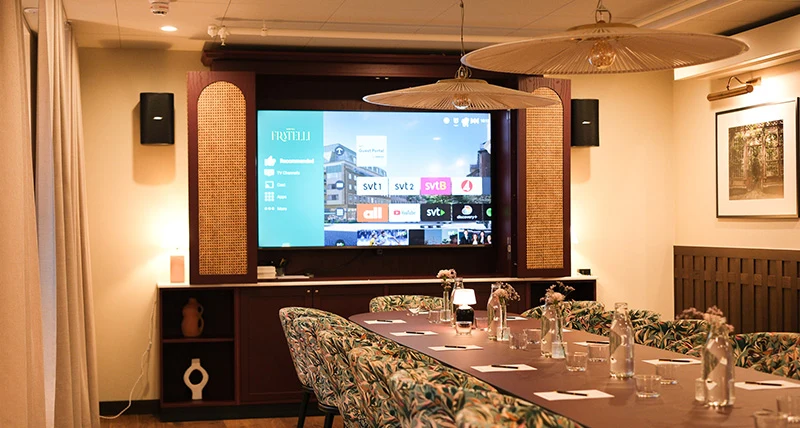 Ett bord med stolar framför en stor tv som hänger på kortväggen