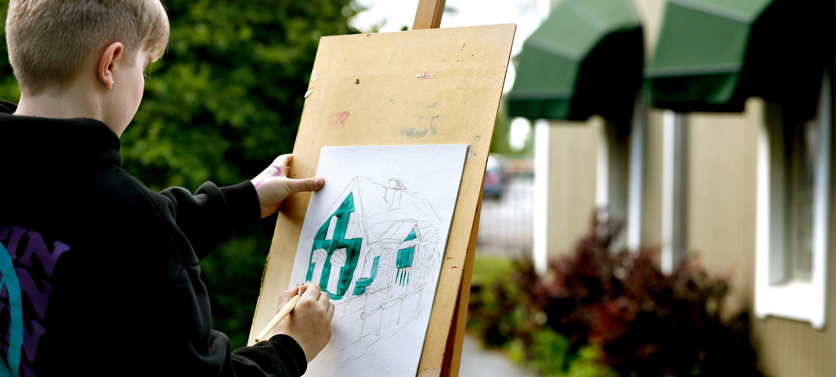 Pojke som målar ett grönt hus på ett straffli utomhus