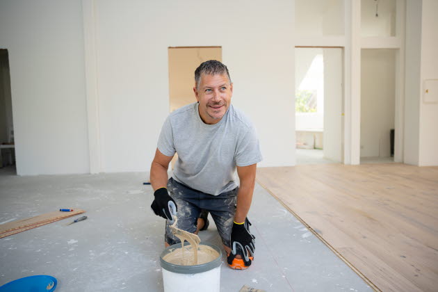 En golvläggare som lägger golv håller i en spatel med lim.