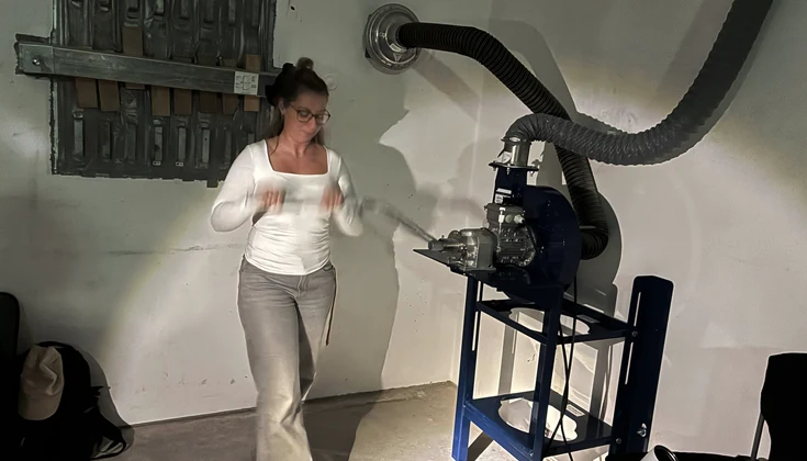 En person står bredvid ventilationsutrustning i ett skyddsrum. En stor fläkt med tillhörande luftkanaler är monterad mot väggen.