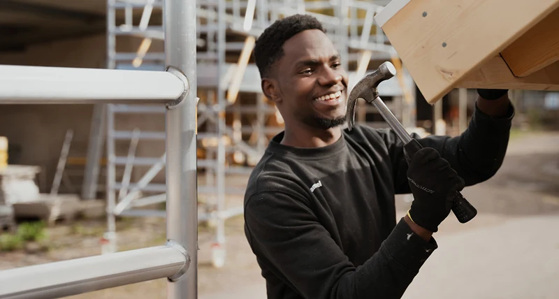 Elev i byggmiljö utomhus, spikar på taket till en lekstuga.