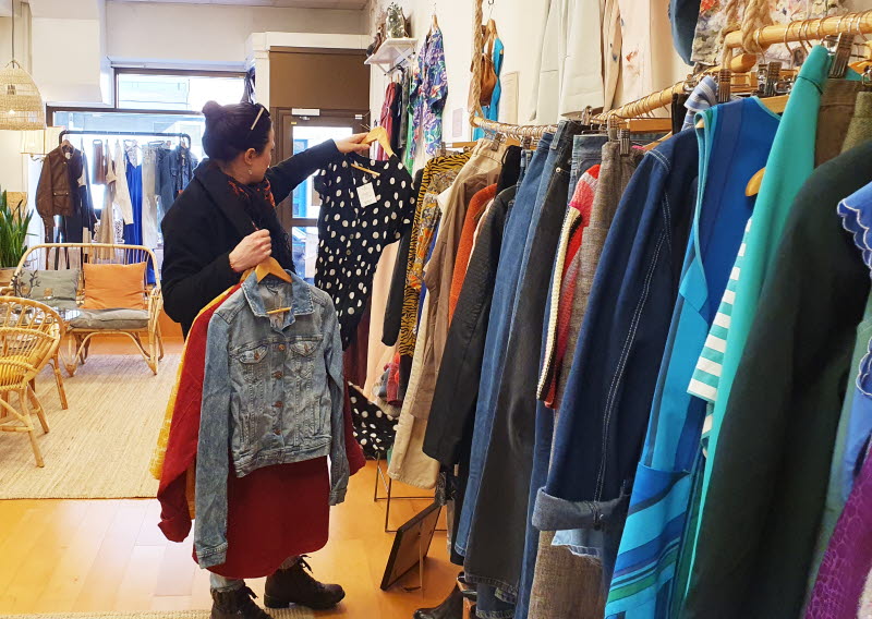 Kvinna tittar på kläder i seond hand butik.