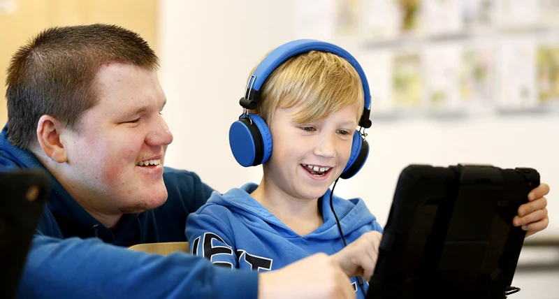 Lärare och yngre elev som sitter med en surfplatta.