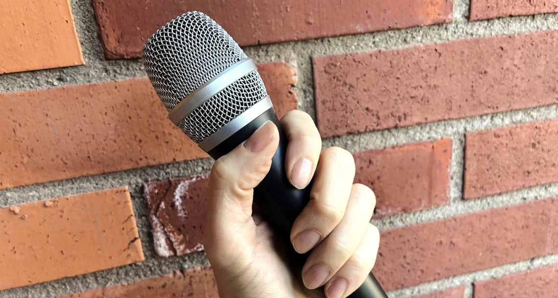 En hand som håller en mikrofon mot en tegelvägg