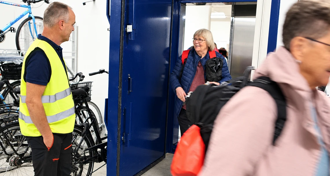 Personer lämnar ett skyddsrum genom en blå skyddsdörr under en övning eller visning. En person i reflexväst står vid utgången och i lokalen syns parkerade cyklar.