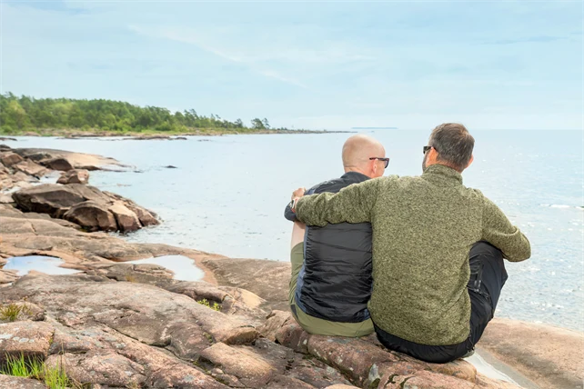 Två män sitter med ryggen mot kameran på klippa vid vatten