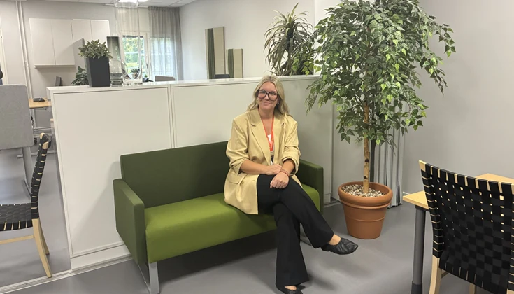 Kvinna som sitter i en grön soffa i pentryt och ler. 