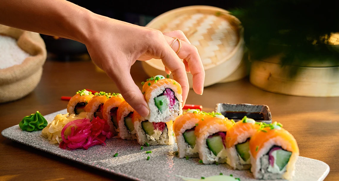 En hand som plockar upp en sushibit från en långsmal bricka.
