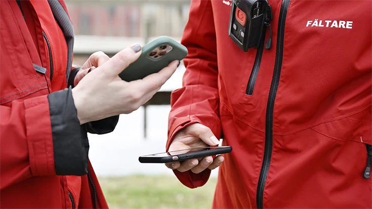Två fältarbetare tittar i var sin mobiltelefon.
