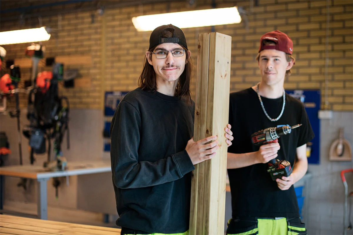 Två leende gymnasieelever i en verkstad.