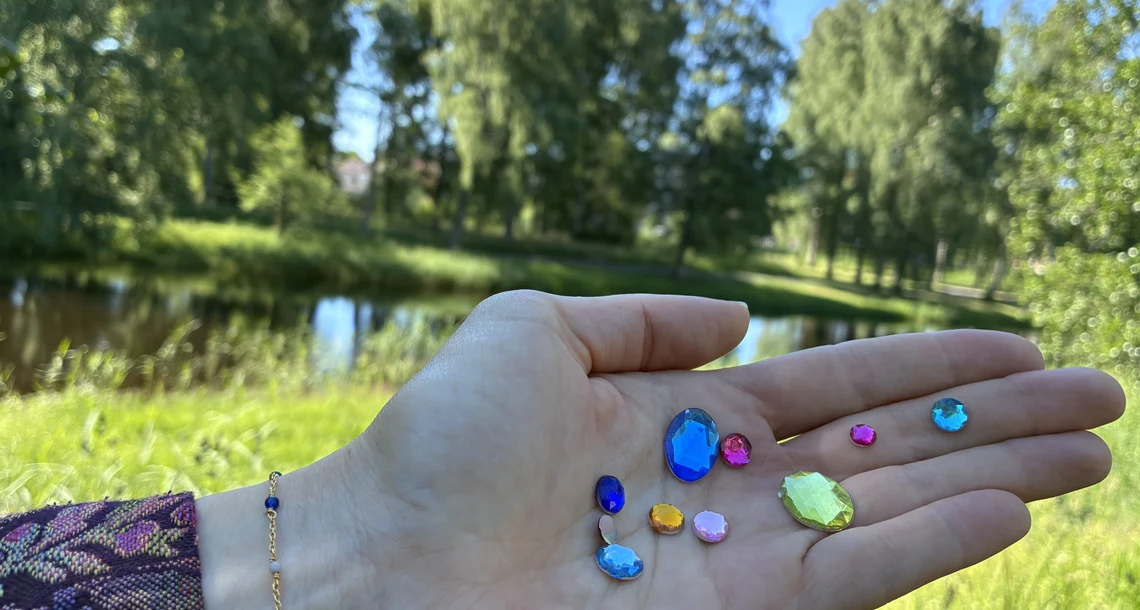 En hand med diamantliknande paljetter sträcks ut framför ett grönområde