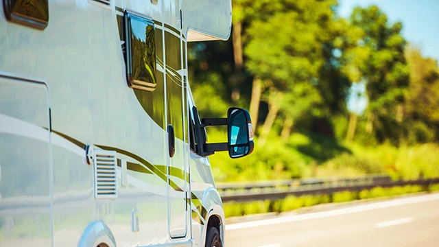 sidan av en vit husbil mot en grönskande bakgrund