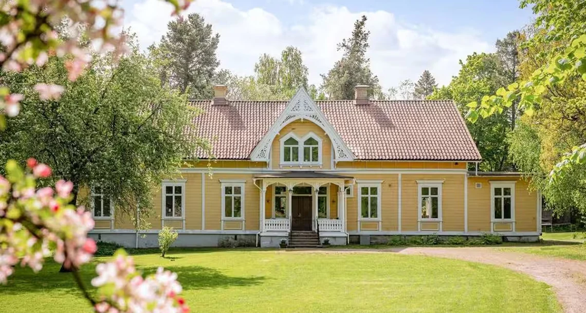 Ett stort gult hus med snirkliga detaljer på fasaden i en lummig trädgård.
