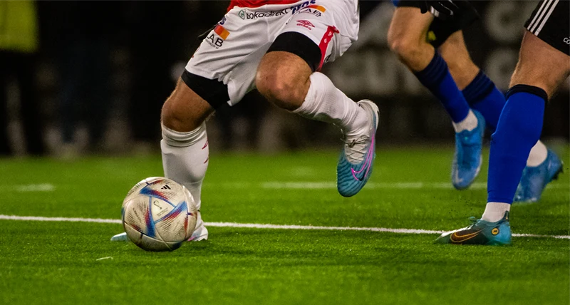 Benen på fotbollspelare med en boll på gräsplan