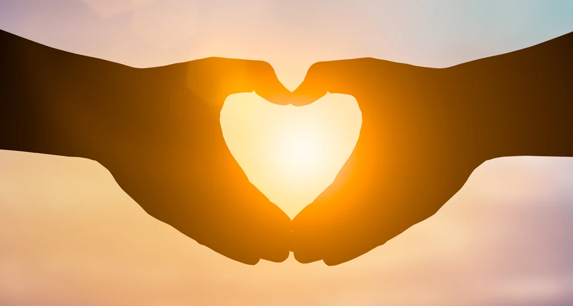 Två händer formar ett hjärta mot solen