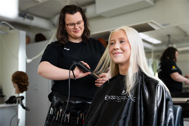 Frisörelev plattar håret på en kund