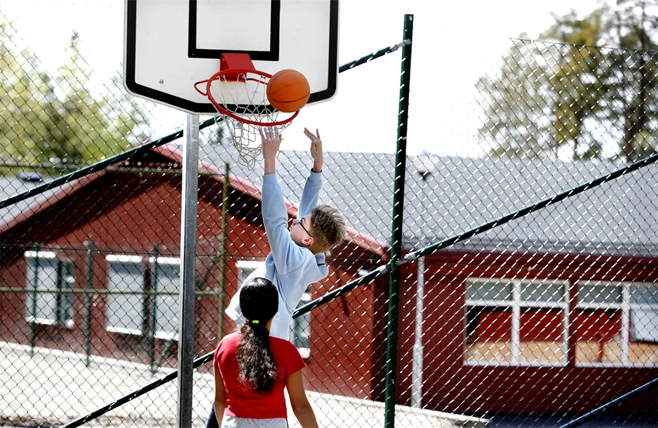 två ungdomar spelar basket på skolgården