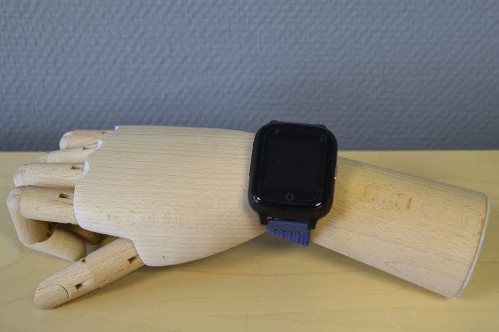 Ett GPS armband som ser ut som en locka som sitter på en konstgjord arm i trä som ligger på ett bord.