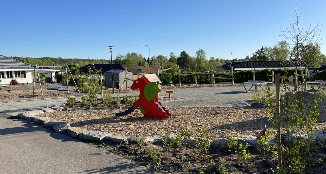 Lekplats utomhus, sandlåda med en röd drake i mitten. 