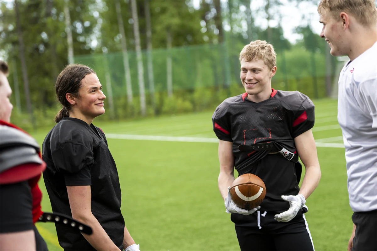 Två gymnasieelever står på en plan för amerikansk fotboll och ler.